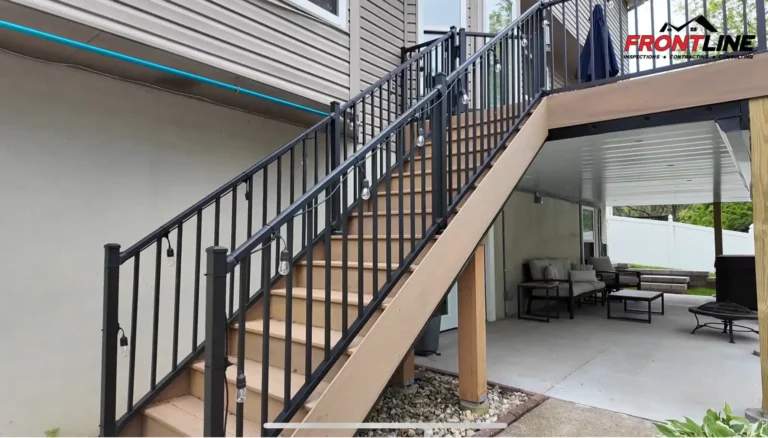 A view of a modern stairway leading up to a covered patio, featuring a black railing with pendant lights. The patio below is furnished with outdoor seating and tables.